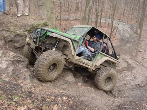 1992 Ford Bronco - A heavily modified off-road vehicle tackles a challenging muddy trail with a driver inside.
