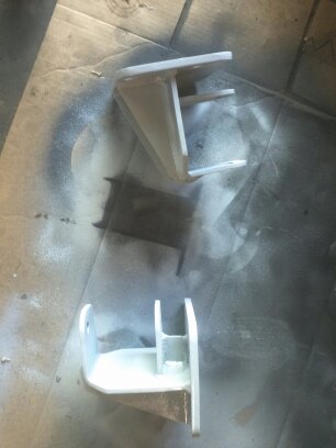 1995 Ford Bronco - Two white metal brackets are shown on a surface that appears to have been used for spray painting.