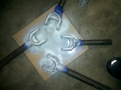 1995 Ford Bronco - Four driveshaft yokes are laid out on cardboard and being spray painted silver.