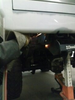 1995 Ford Bronco - A person welds the frame of a white vehicle that is supported by jack stands.