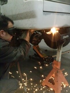 1995 Ford Bronco - A person is welding on the underside of a vehicle, with sparks illuminating the area.