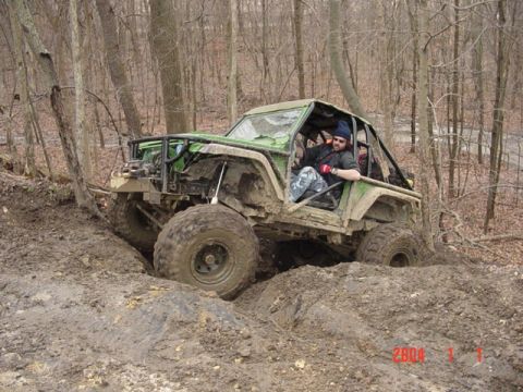 1992 Ford Bronco - An off-road vehicle navigates a challenging muddy terrain in a wooded area.