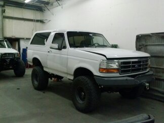 1995 Ford Bronco - A white Ford Bronco with a lifted suspension sits in a garage, with another vehicle partially visible to the left.