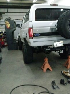 1995 Ford Bronco - Rear view of a white 1995 Ford Bronco, lifted and supported by jack stands in a workshop.