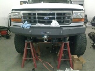 1995 Ford Bronco - Front view of a white Ford Bronco with an aftermarket bumper, supported by jack stands in a garage.