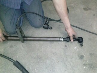 1995 Ford Bronco - A person is working on a tie rod assembly, possibly for a vehicle repair or modification.