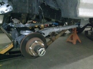 1995 Ford Bronco - Close-up view of the vehicle's front axle and suspension system, with parts supported by jack stands.