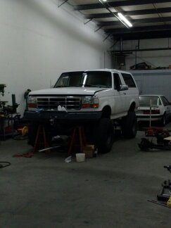 1995 Ford Bronco - A white Ford Bronco is elevated on jack stands inside a garage, with tools and equipment scattered around.