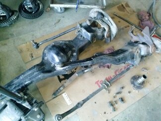 1995 Ford Bronco - Disassembled front axle and differential components, likely for a Ford Bronco, are laid out on a workshop floor.
