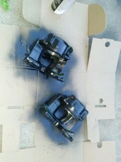 1995 Ford Bronco - Two brake calipers are being painted black on a cardboard surface. The SuperMotors logo is visible at the bottom.
