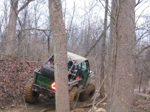 1992 Ford Bronco - A custom off-road vehicle navigates a challenging, wooded trail with muddy terrain.
