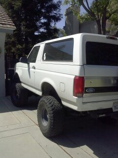 1995 Ford Bronco - This white SUV is parked on a paved surface next to a building and trees.