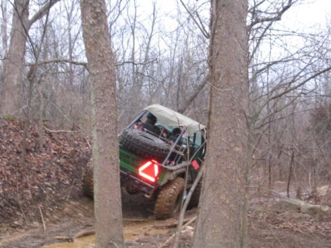 1992 Ford Bronco - An off-road vehicle navigates a challenging muddy trail in a wooded area.