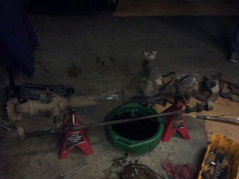 1995 Ford Bronco - Front axle assembly, likely from a truck or SUV, is supported by jack stands with an oil drain pan beneath.