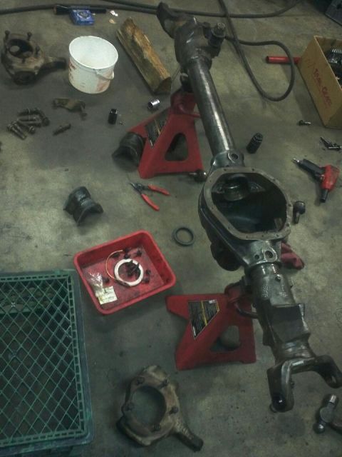 1995 Ford Bronco - Front axle assembly disassembled on the floor with tools and parts nearby.