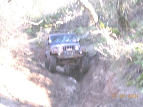 1994 Ford Bronco - A blue Jeep Wrangler navigates a challenging muddy off-road path.