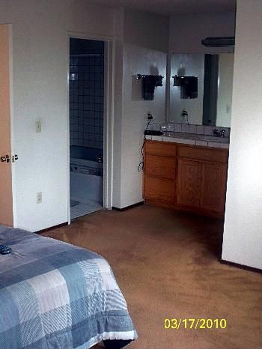 Bedroom with a blue and white checkered bedspread and a bathroom with a vanity and bathtub visible
