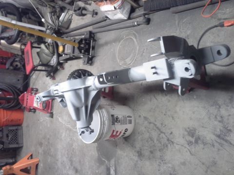 1968 Ford Bronco - Gray painted rear axle assembly on a garage floor, supported by a bucket and jack stands.