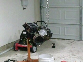 1995 Ford Bronco - Engine being worked on, suspended from a chain hoist in a garage.