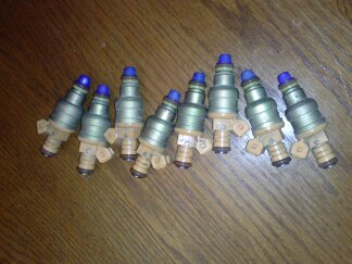 1995 Ford Bronco - A set of eight fuel injectors, likely for a performance engine build, are displayed on a wooden table.