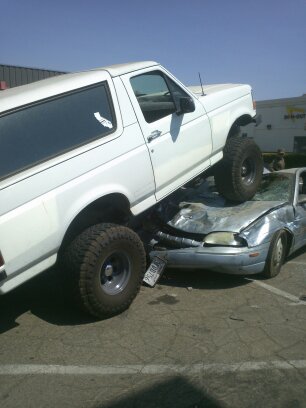 1995 Ford Bronco - A white Ford Bronco is perched atop a severely damaged silver sedan.