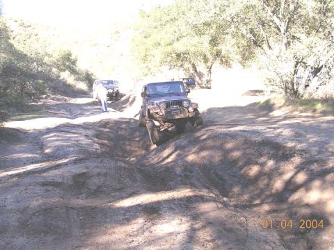 1994 Ford Bronco - Two off-road vehicles traverse a challenging dirt path on a sunny day.