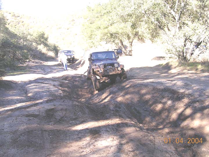 Lifted Jeep Wrangler with winch dropping into a rutted dirt trail washout