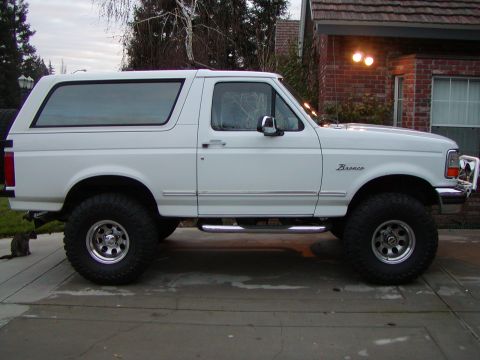 1995 Ford Bronco - This white Ford Bronco is parked outside a brick house. It has a lifted suspension and side steps.