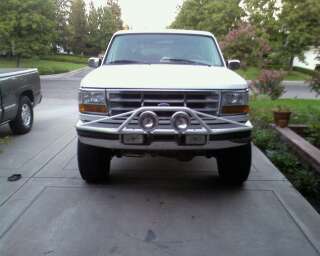 1995 Ford Bronco - A white Ford Bronco is parked in front of a house, with a dark-colored truck to its left.