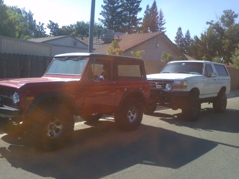 1995 Ford Bronco - Two Ford Broncos, one older model and one newer, are parked side-by-side on a sunny day.