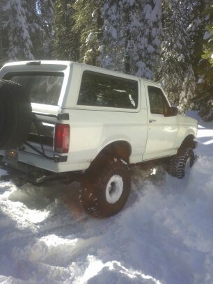 1995 Ford Bronco - A white 1995 Ford Bronco navigates a snowy forest road, its spare tire mounted on the back.