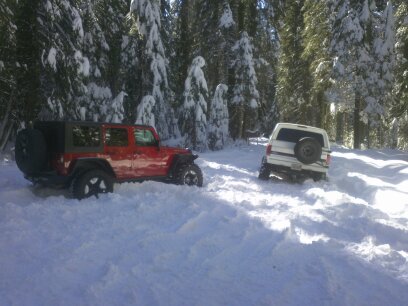 1995 Ford Bronco - Two off-road vehicles are stuck in deep snow in a wooded area.
