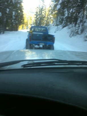 1995 Ford Bronco - A blue pickup truck drives down a snow-covered road, viewed from the perspective of another vehicle.