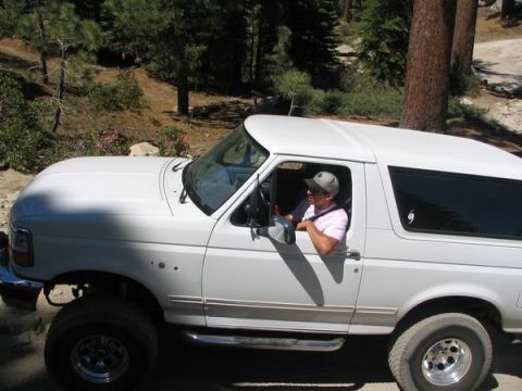 1995 Ford Bronco - A white 1995 Ford Bronco navigates an off-road trail with a driver at the wheel.