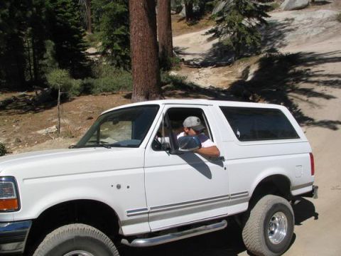 1995 Ford Bronco - A white Ford Bronco navigates a dirt road in a wooded, rocky area.