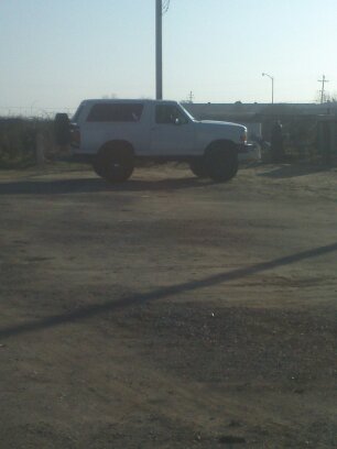 1995 Ford Bronco - A white Ford Bronco is parked on a dirt lot under a clear sky.