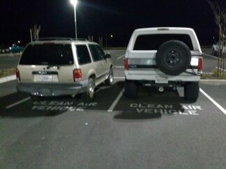 1995 Ford Bronco - Two SUVs are parked in a lot at night, with one a spare tire on its rear.
