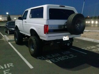 1995 Ford Bronco - Rear view of a white 1995 Ford Bronco, lifted with large tires, parked in a lot at dusk.