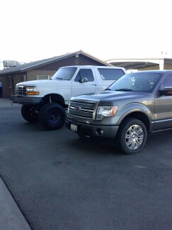 1995 Ford Bronco - Two trucks are parked side-by-side in a paved lot with a building in the background.