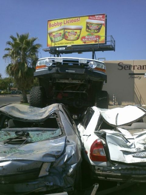 1995 Ford Bronco - A lifted truck looms over two severely damaged cars, with a billboard advertising dips overhead.
