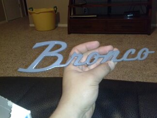 1995 Ford Bronco - A person holds a gray Bronco emblem in front of a couch and entertainment center.