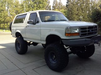1995 Ford Bronco - This lifted 1995 Ford Bronco is parked on a paved driveway with trees in the background.