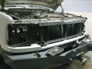 1995 Ford Bronco - Front end of a white truck undergoing repair, with the hood open and grille removed, revealing the engine compartment.