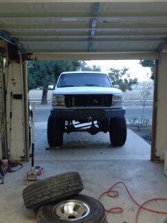 1995 Ford Bronco - A white pickup truck with a lifted suspension and oversized tires is positioned in a garage doorway.
