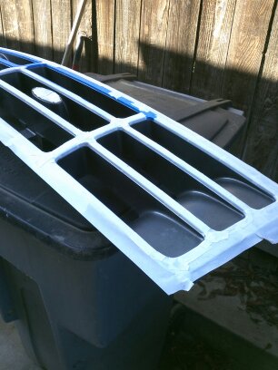 1995 Ford Bronco - A taped 1995 Ford Bronco grille is prepared for painting, showing its distinctive horizontal bars and central emblem.