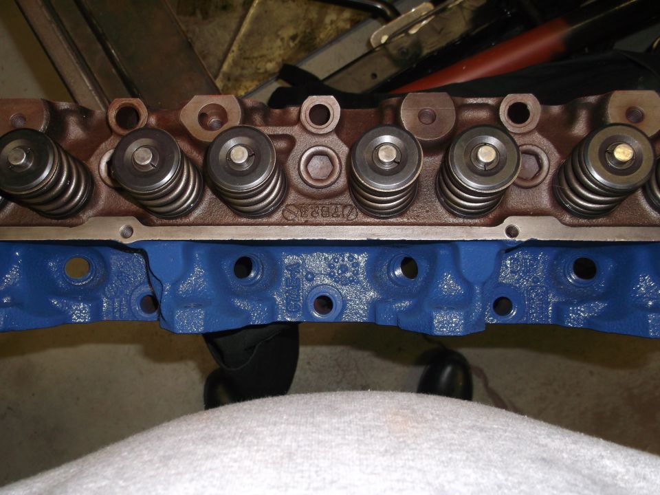 Cylinder head with valve springs installed on a blue-painted engine block in a garage