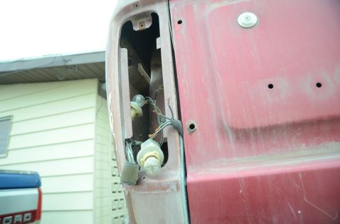 1979 Ford Bronco - The rear of a red 1979 Ford Bronco shows exposed tail light wiring and sockets, with a blue truck visible to the left.