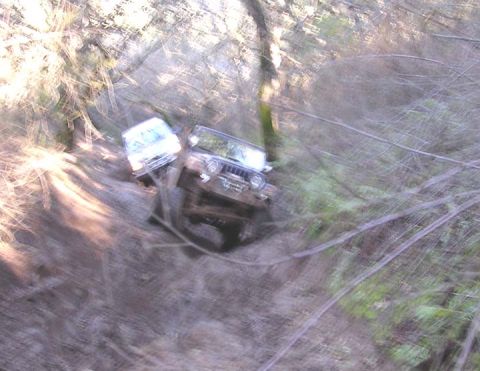 1994 Ford Bronco - A blurry, motion-affected overhead shot of two vehicles on a muddy off-road trail in wooded terrain; the foreground vehicle is a boxy SUV w…
