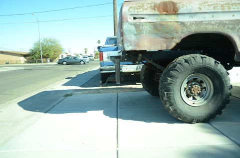 1979 Ford Bronco - A close-up view of a heavily modified vehicle's rear tire and rusty bed, parked alongside another truck.