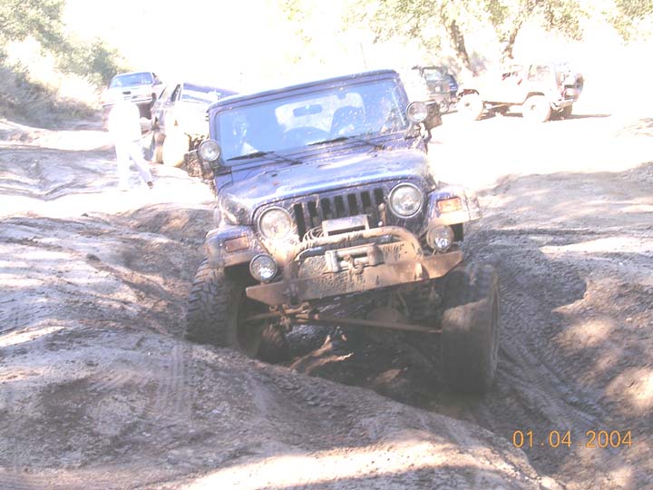 Muddy dark Jeep Wrangler with winch and tube bumper dropping into a rutted mud trough